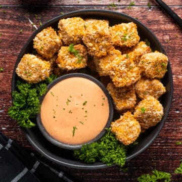 Vegan chicken nuggets stacked up on a plate with fresh parsley and a bowl of yum yum sauce.