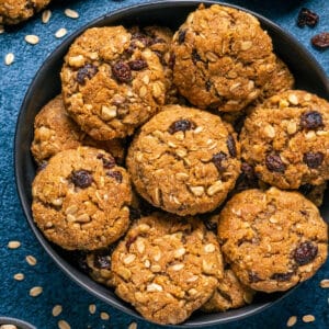 Vegan oatmeal raisin cookies stacked up on a black plate.