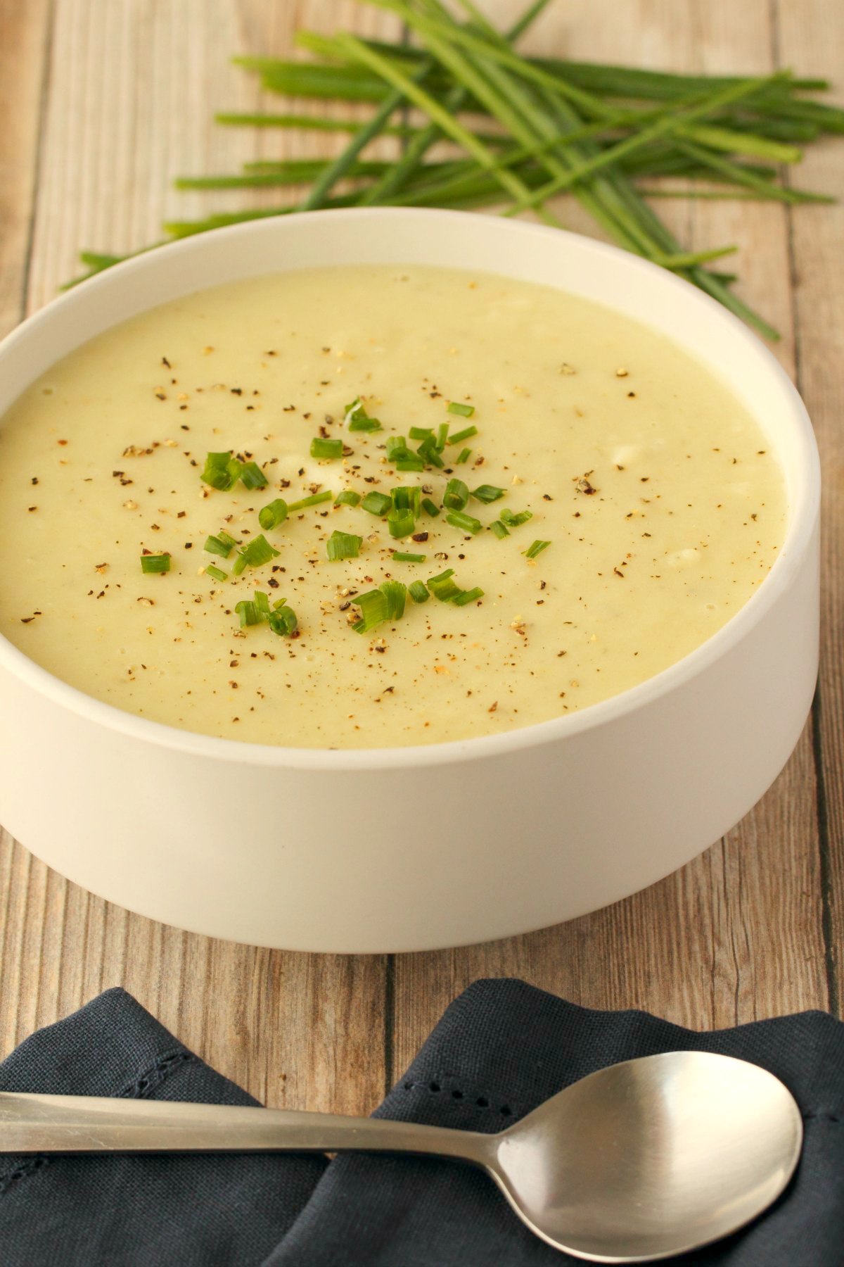 Vegan potato leek soup topped with chopped chives in a white bowl.