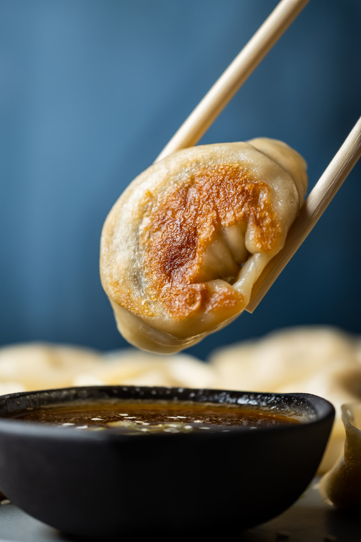 Chopsticks holding a dumpling above a bowl of dipping sauce.