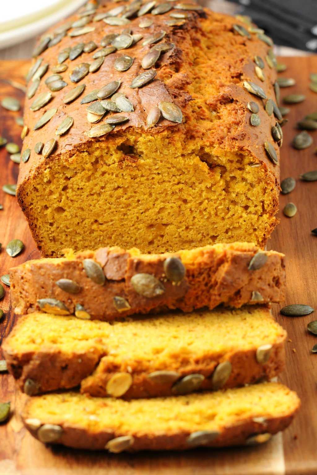 Sliced vegan pumpkin bread topped with pumpkin seeds on a wooden board.