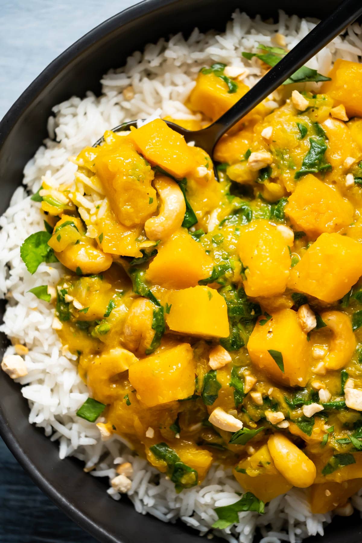 Thai pumpkin curry with rice in a black bowl with a spoon.