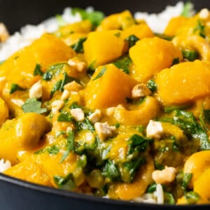 Vegan pumpkin curry with rice in a black bowl.