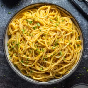 Vegan pumpkin pasta in a bowl topped with chopped parsley and ground black pepper.