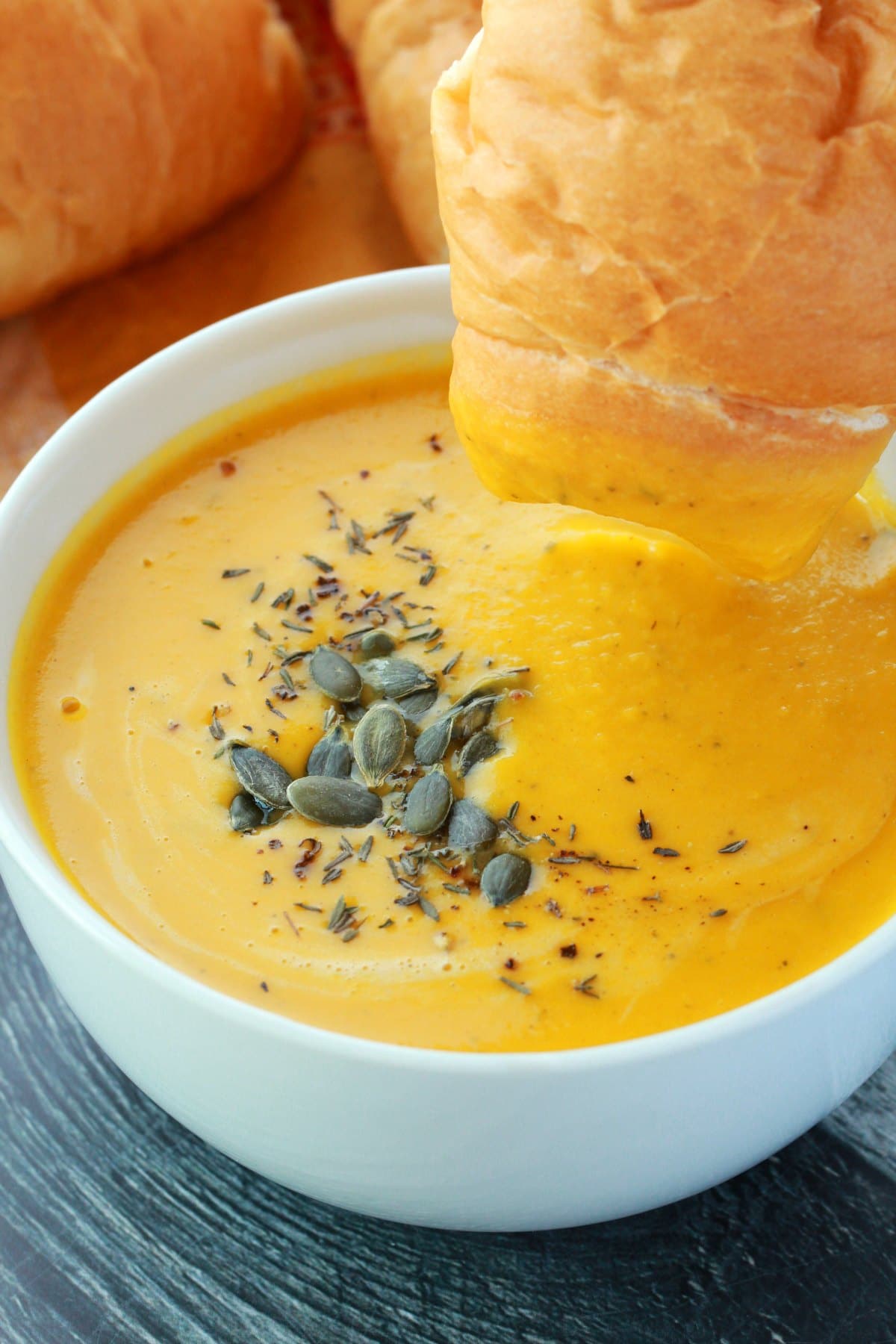 Vegan pumpkin soup topped with dried thyme and pumpkin seeds in a white bowl. 