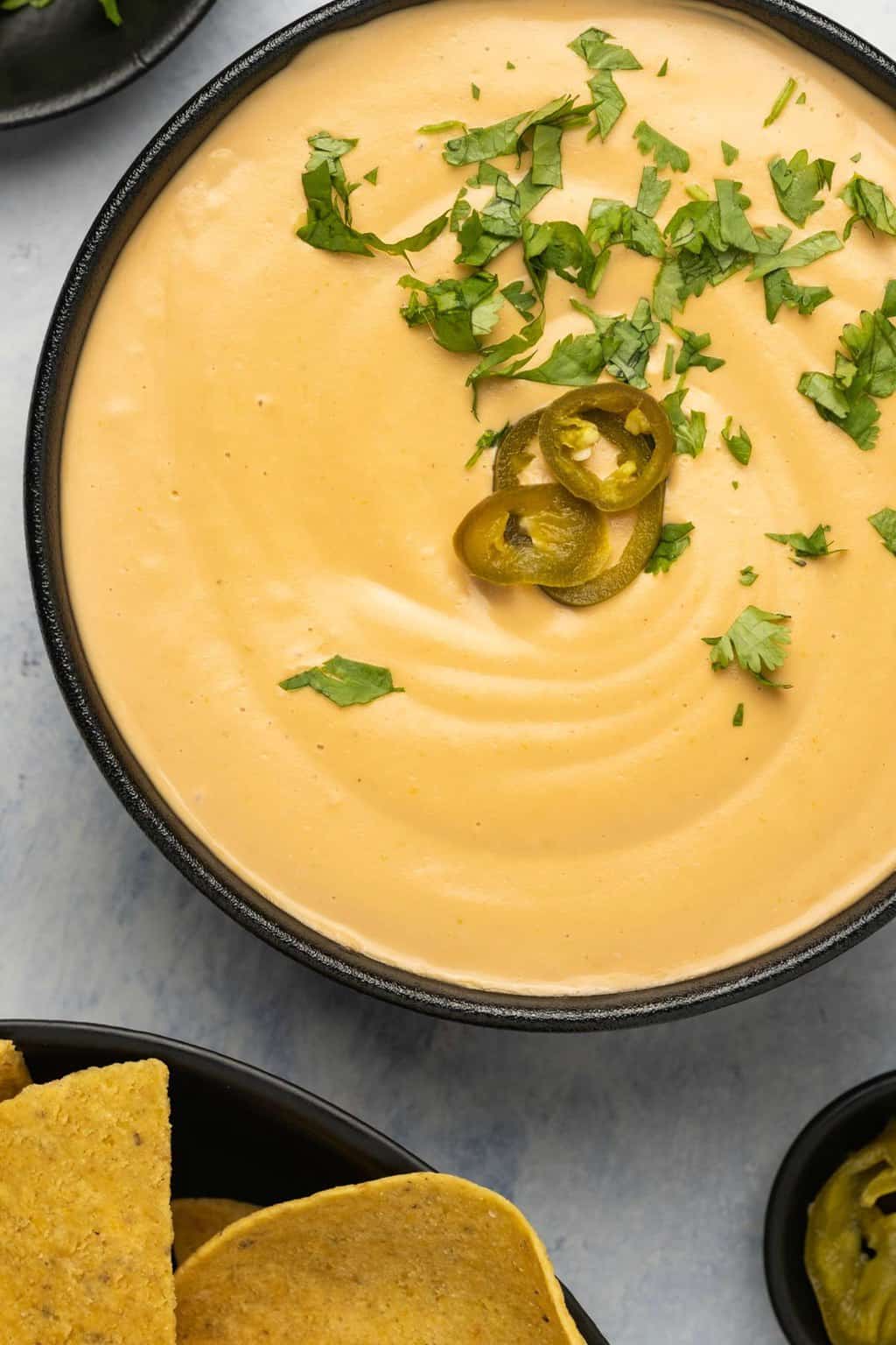 Vegan queso topped with sliced jalapeños and chopped cilantro in a black bowl. 