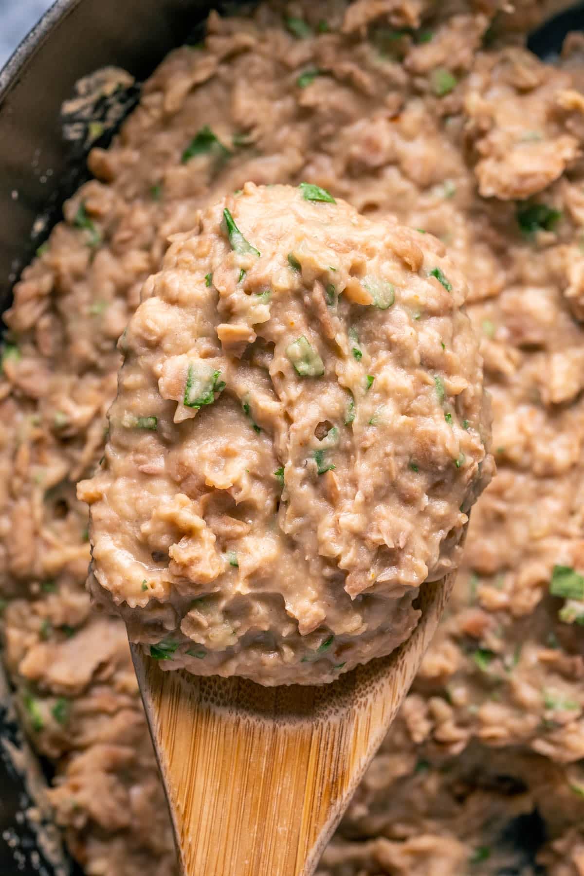 Vegan refried beans in a pot with a wooden spoon.