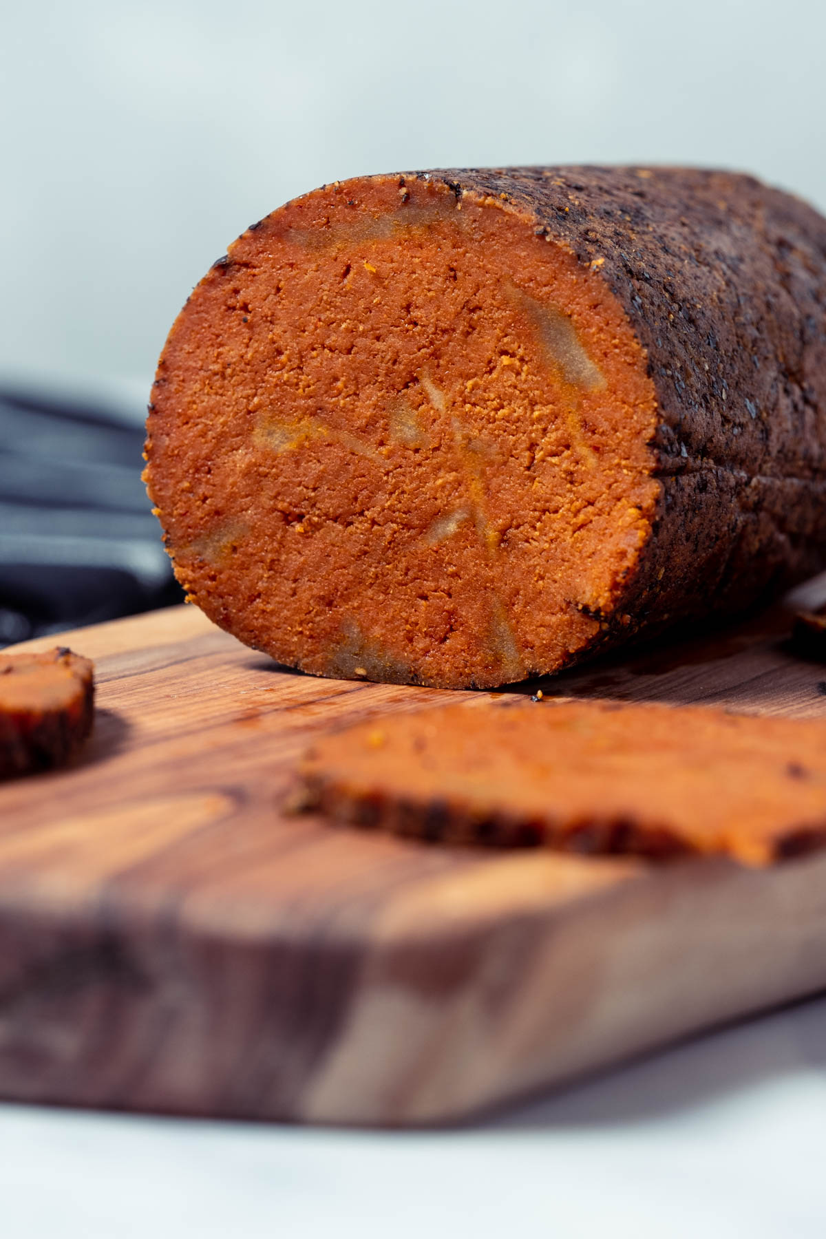 A roll of sliced vegan salami on a wooden board.