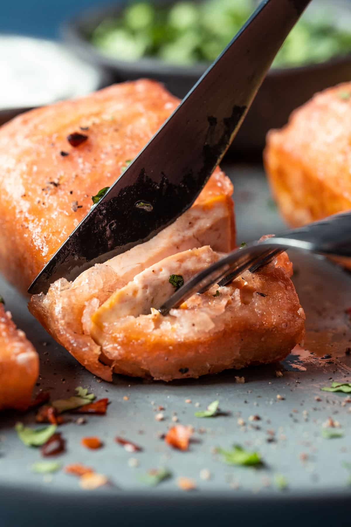 Cutting into a piece of vegan salmon with a knife and fork.