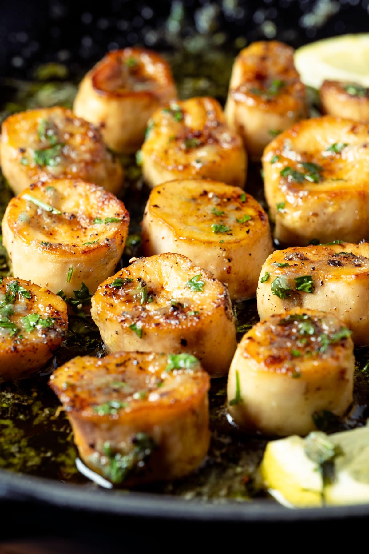 Vegan scallops with lemon slices and parsley in a frying pan.