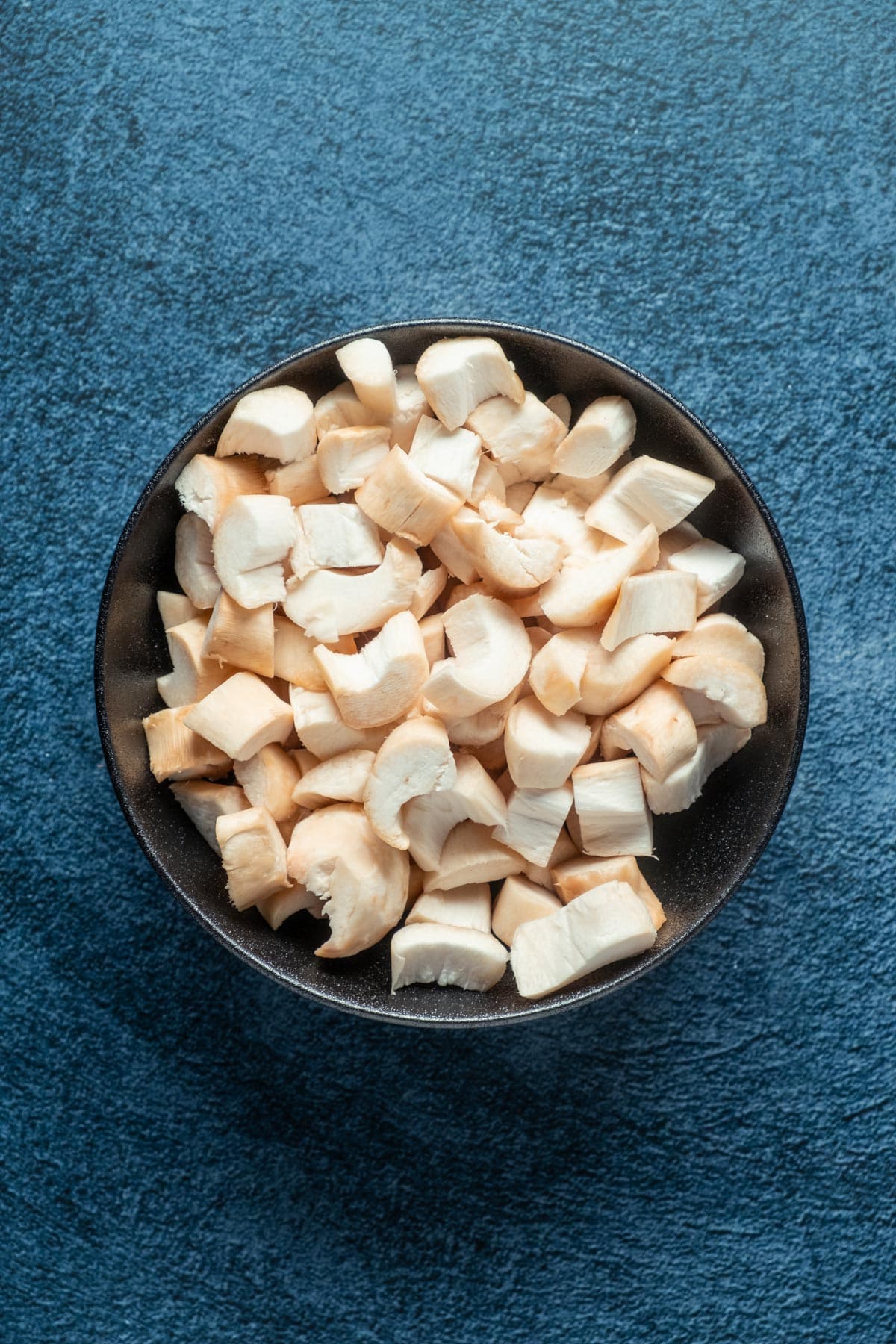 Sliced king oyster mushrooms in a black bowl.