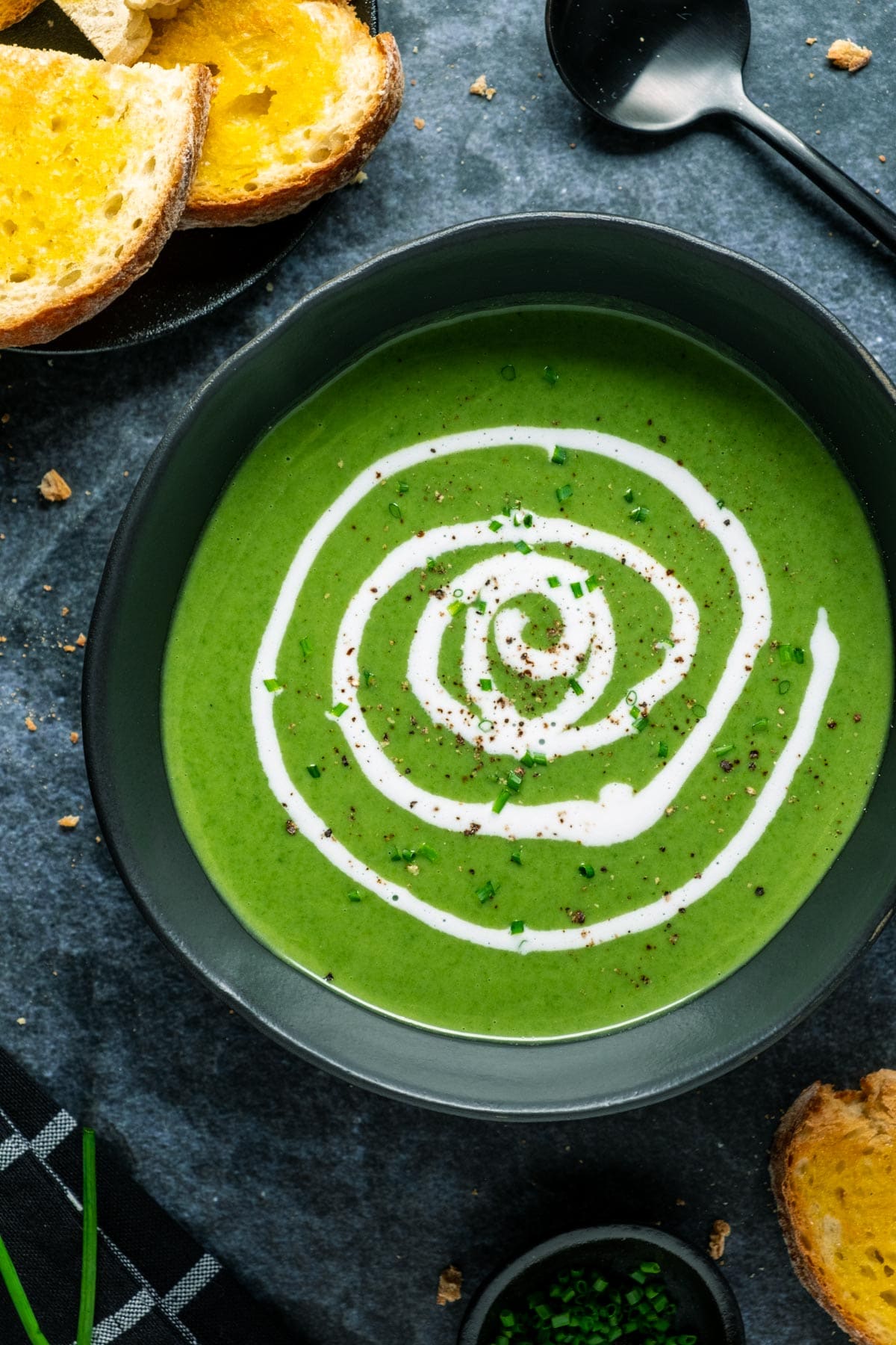 Vegan spinach soup in a black bowl with a swirl of coconut cream on top. 