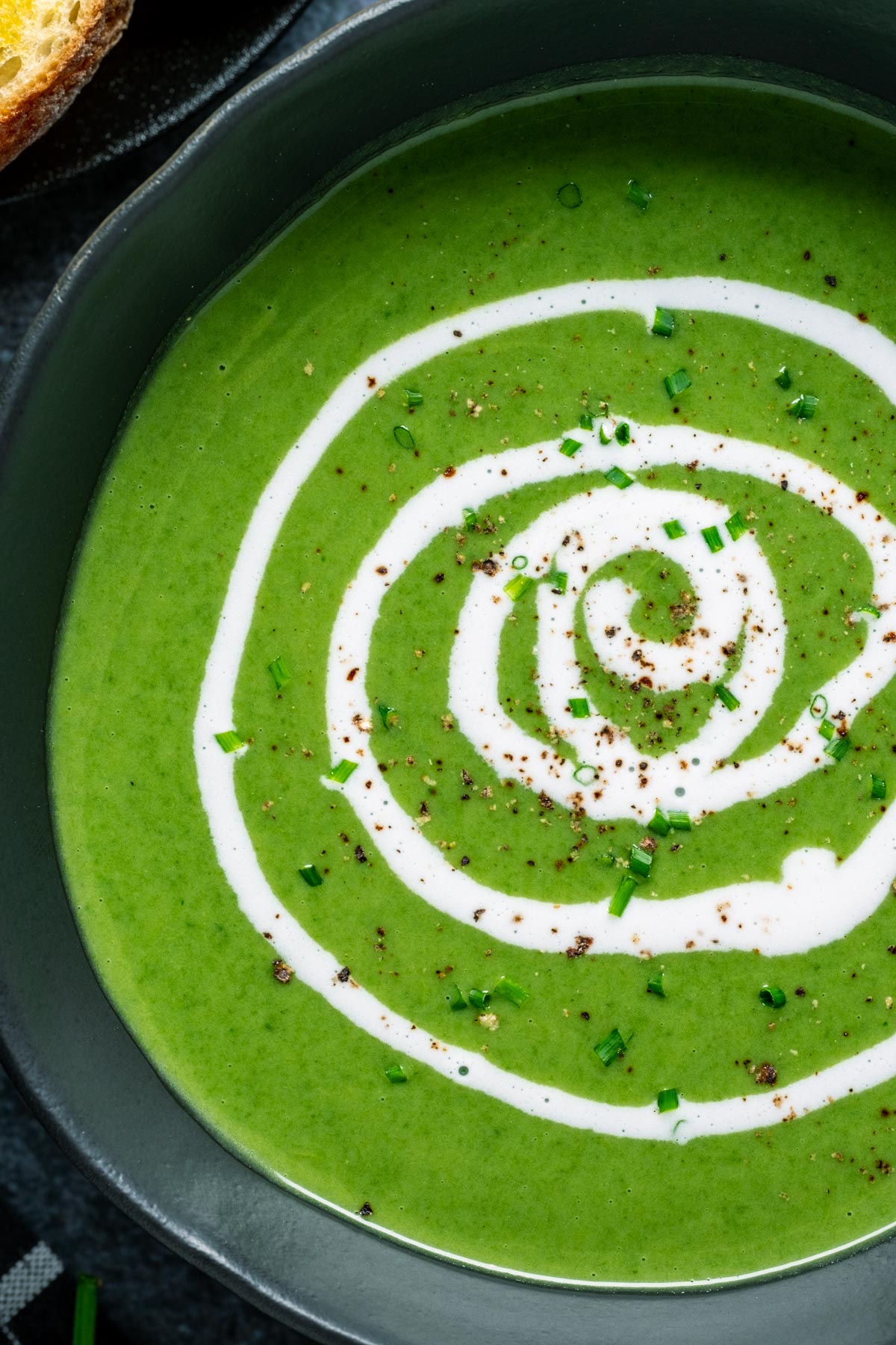 Vegan spinach soup in a black bowl with a swirl of coconut cream on top.