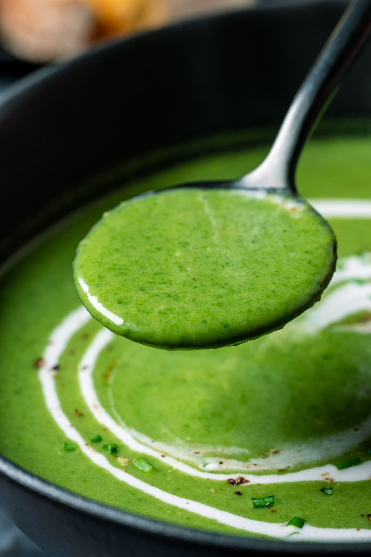 Vegan spinach soup in a black bowl with a spoon.