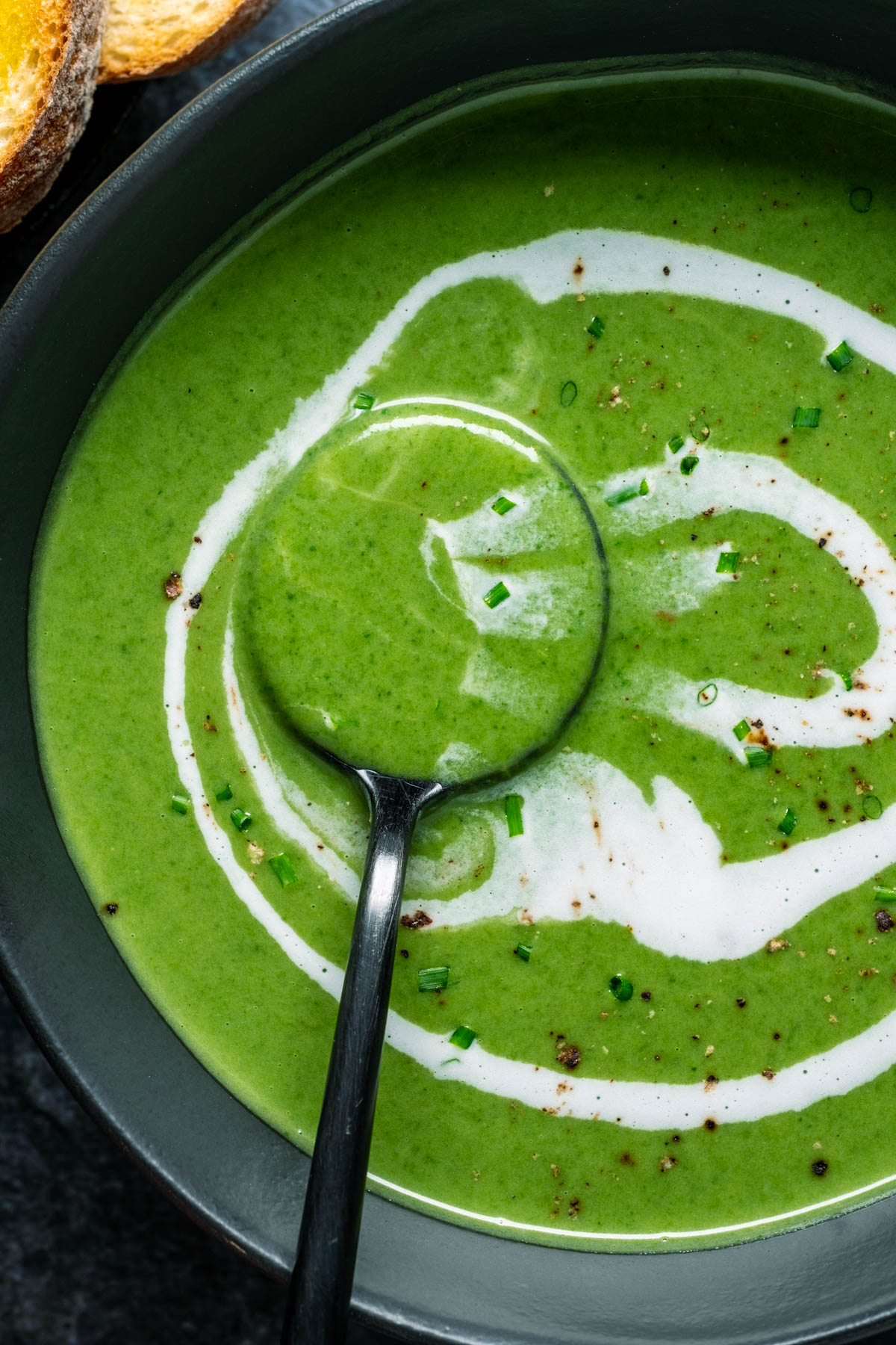 Vegan spinach soup in a black bowl with a swirl of coconut cream and a spoon.