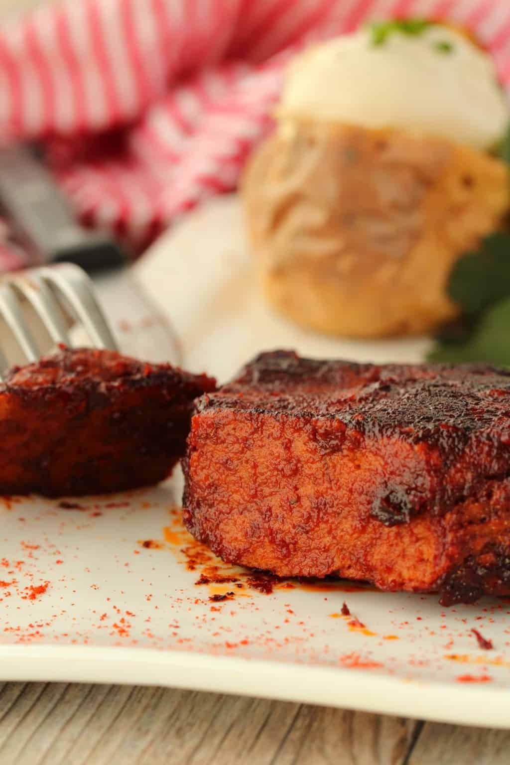 Vegan Steak on a white plate with a piece cut out of it. 