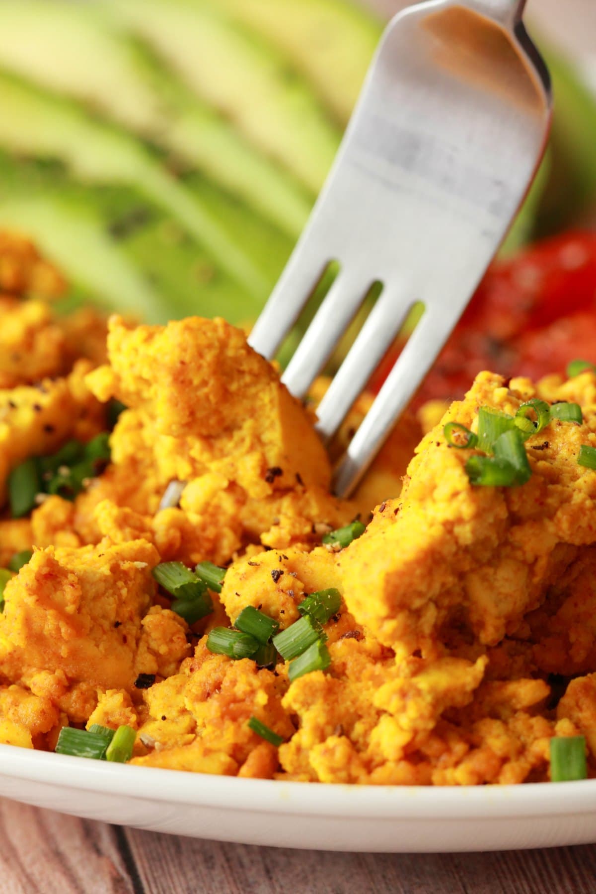 Tofu scramble topped with chopped chives on a white plate with a fork. 