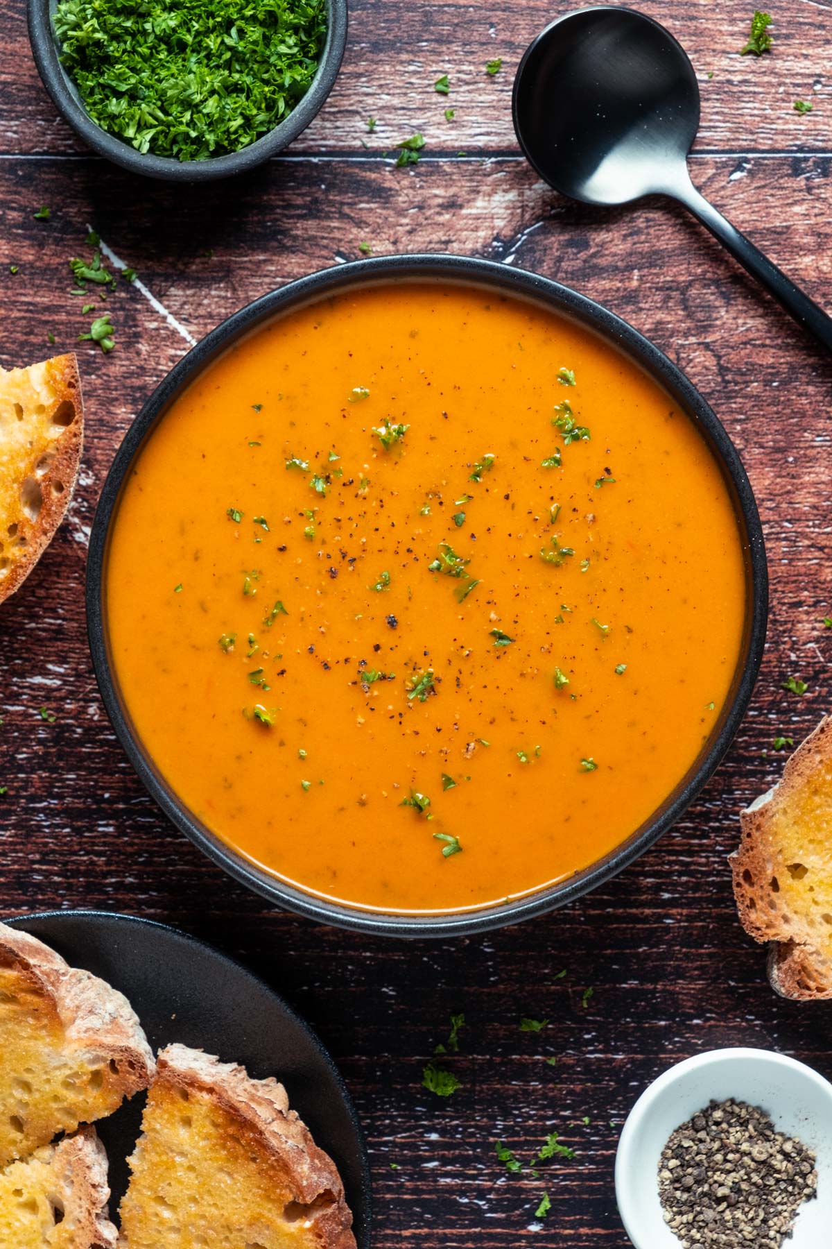 Vegan tomato soup topped with fresh chopped parsley in a black bowl.