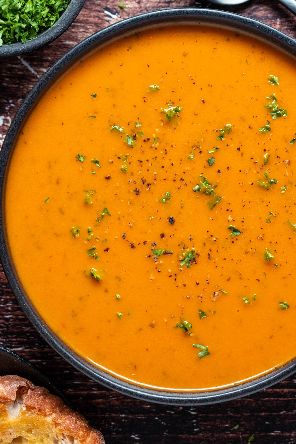 Vegan tomato soup topped with fresh chopped parsley in a black bowl.