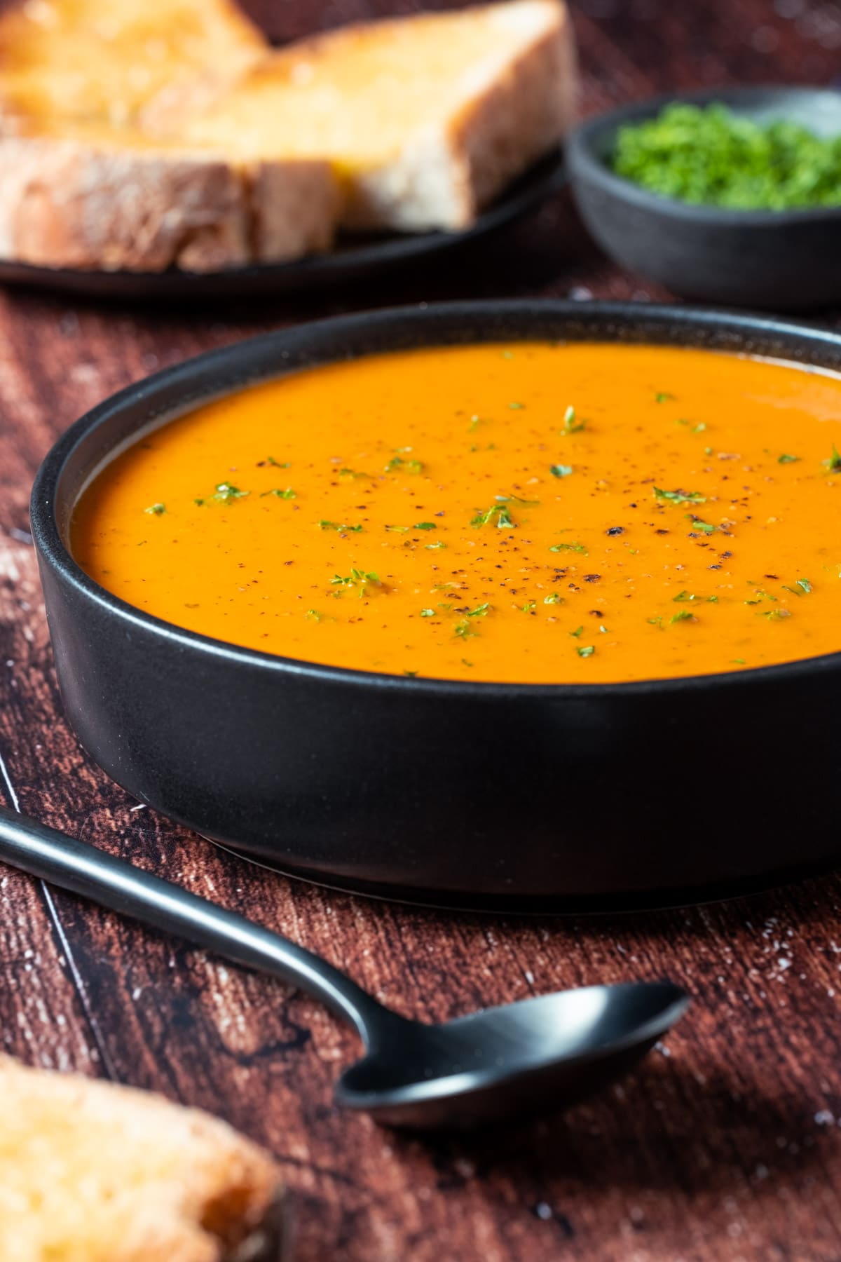 Vegan tomato soup topped with fresh chopped parsley in a black bowl.