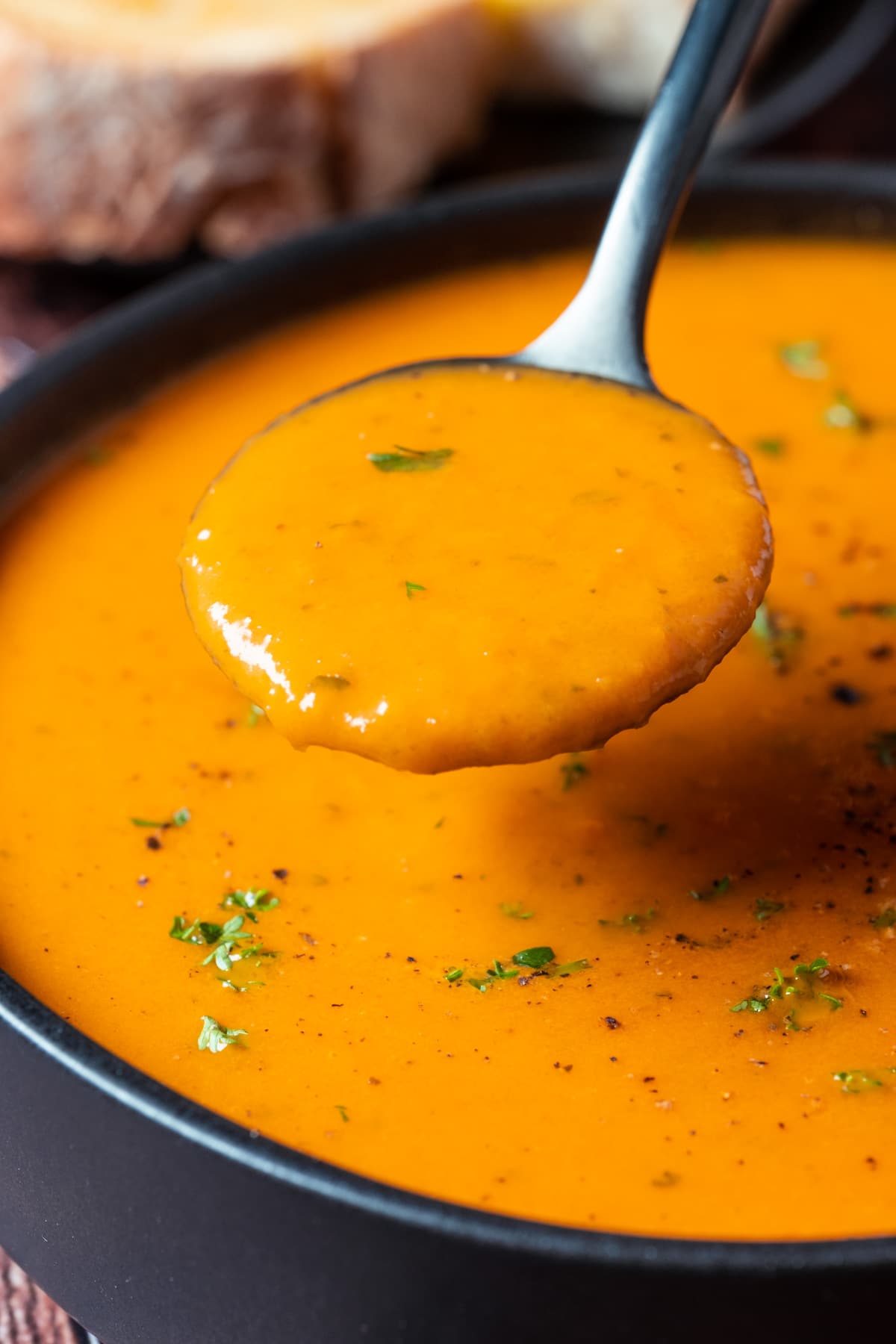 Vegan tomato soup topped with fresh chopped parsley in a black bowl with a spoon.