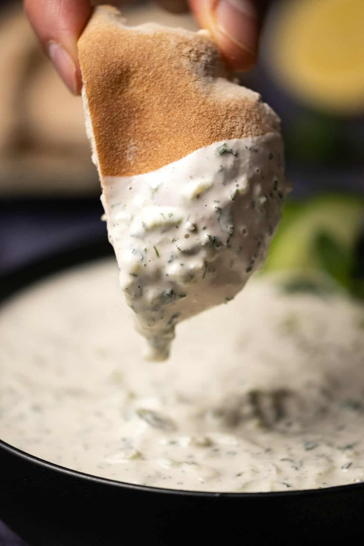 Pita bread dipping into a bowl of tzatziki. 