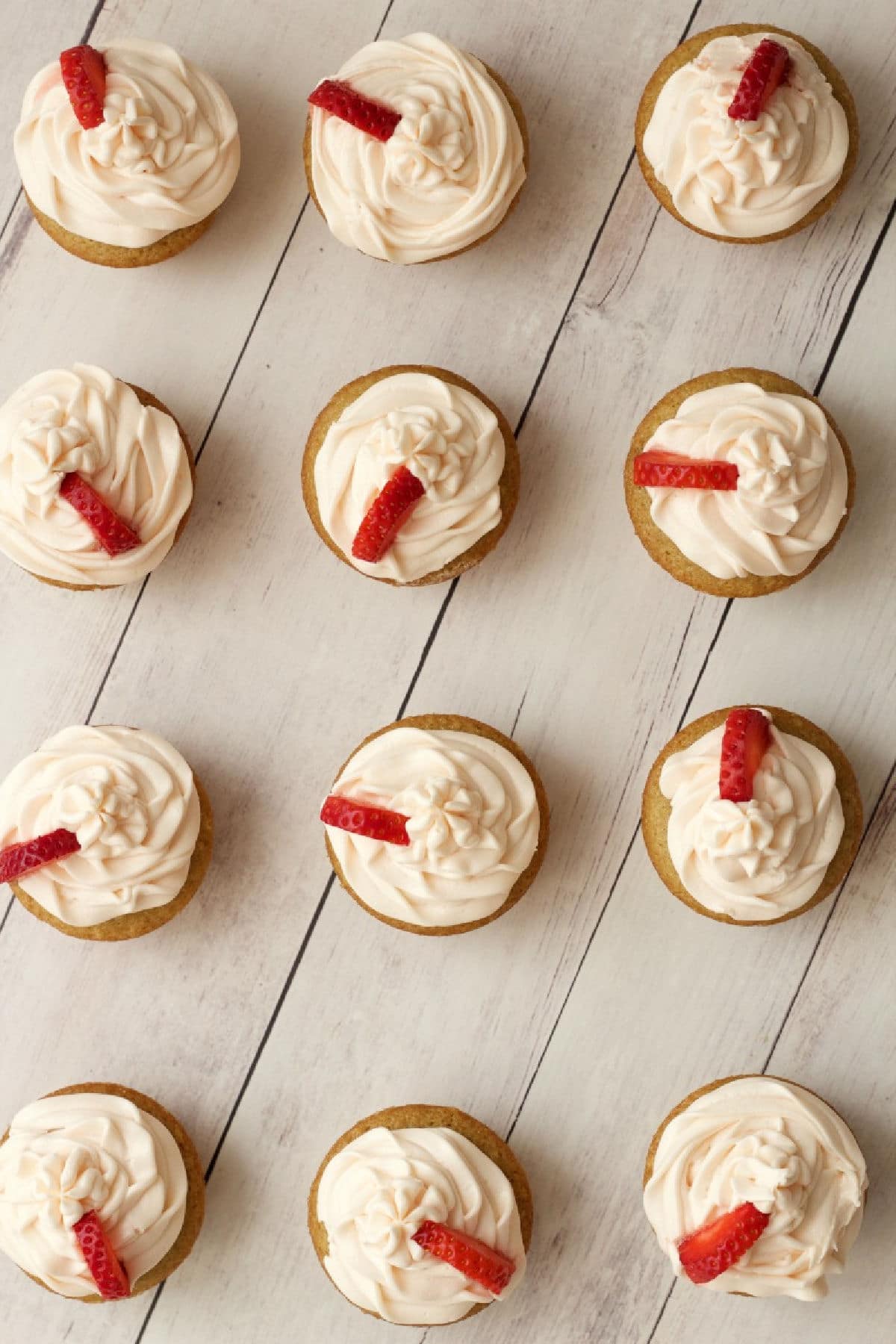 Vanilla cupcakes topped with frosting and fresh strawberries. 