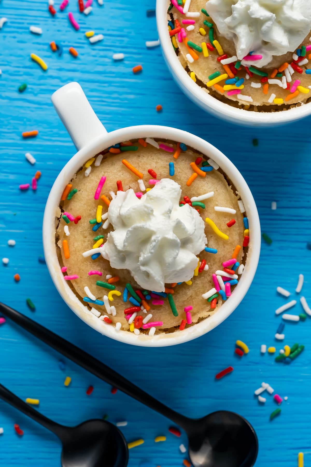 Vegan vanilla mug cake in a white mug topped with sprinkles and whipped cream.