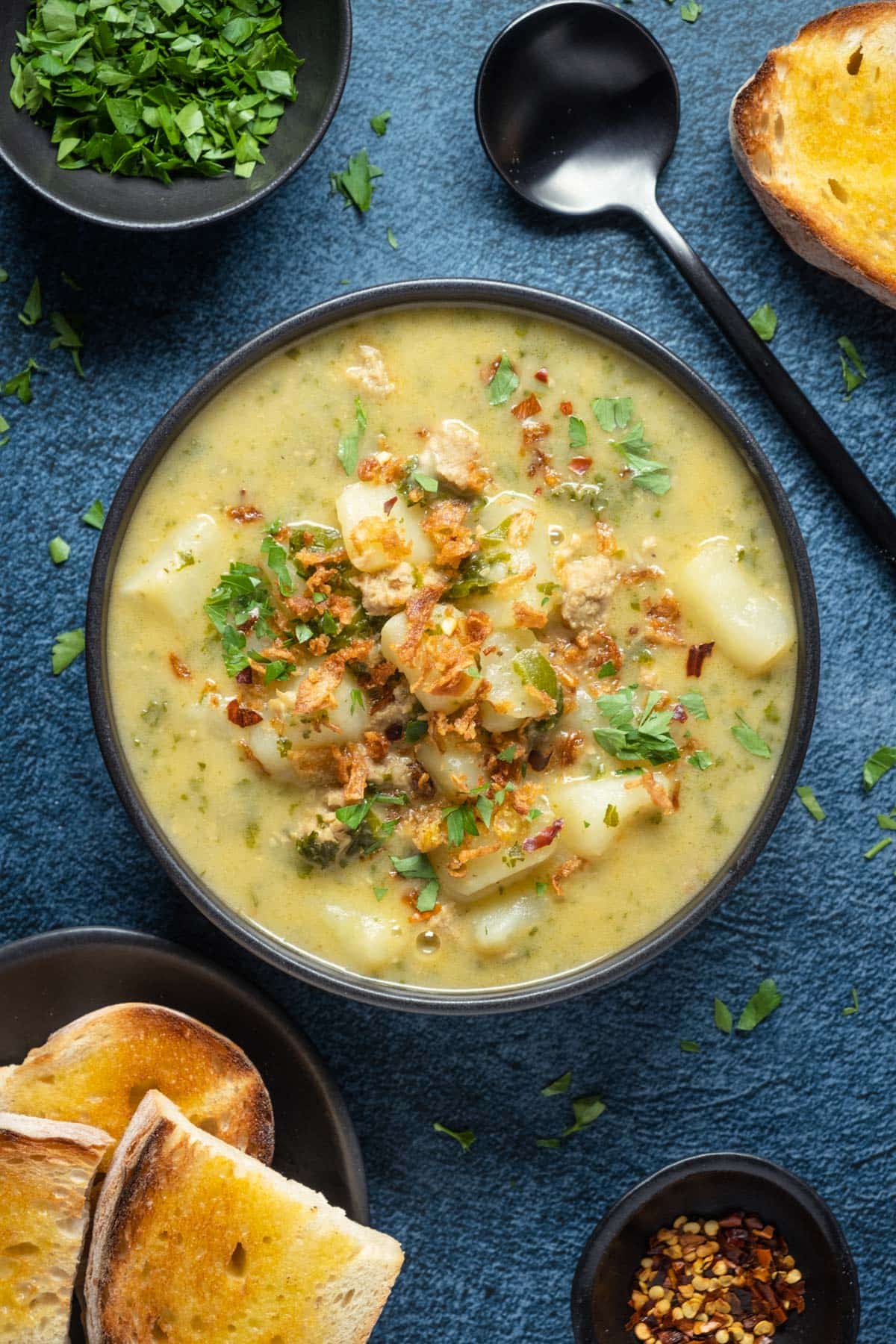 Vegan zuppa toscana topped with crispy fried onions and parsley in a black bowl. 