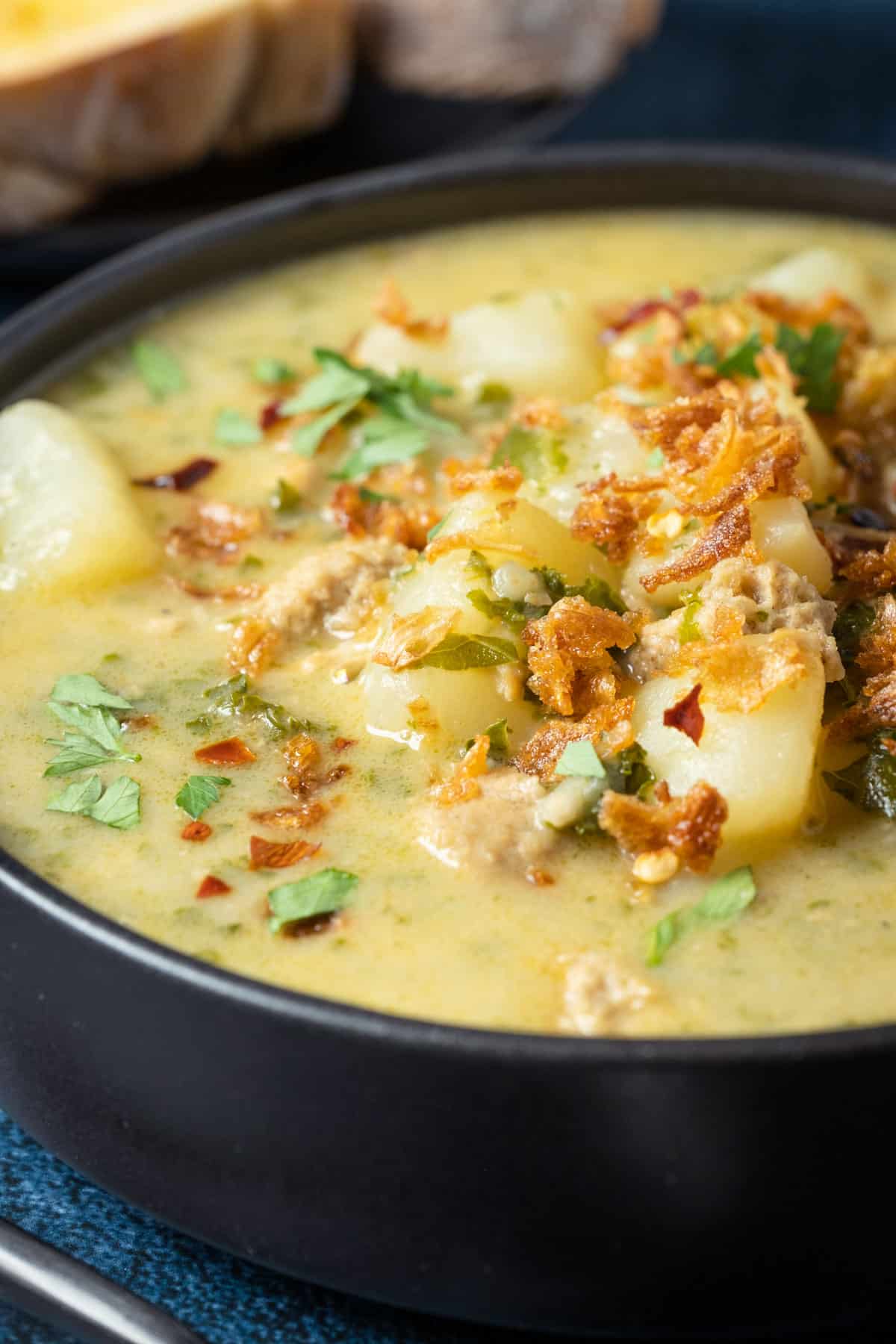 Vegan zuppa toscana topped with crispy fried onions and parsley in a black bowl.